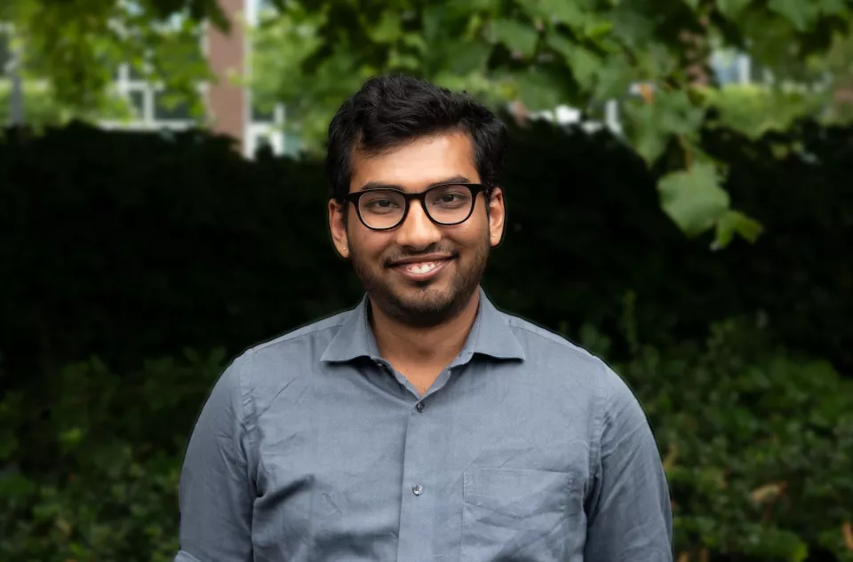 A man with black hair, beard and glasses smiling