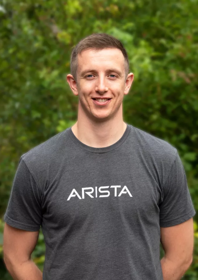 A man in a grey top smiling and standing outside