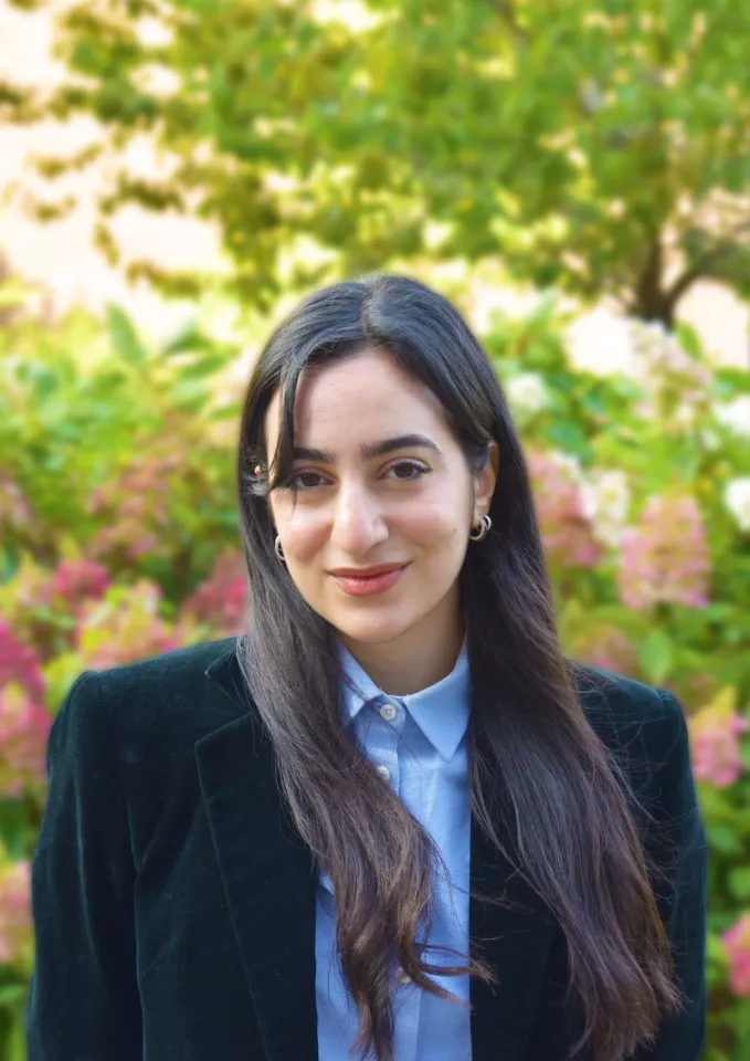 A dark haired woman wearing a black blazer and blue shirt posing