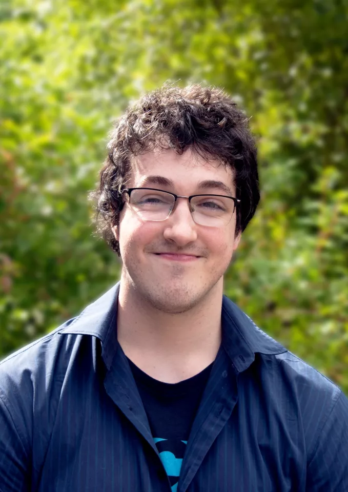 A man with dark hair and glasses standing and smiling