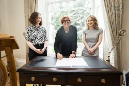 Kerstin Mey, then-president, signing document with two women on either side of her