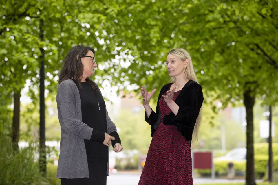 Two women talking in front of trees