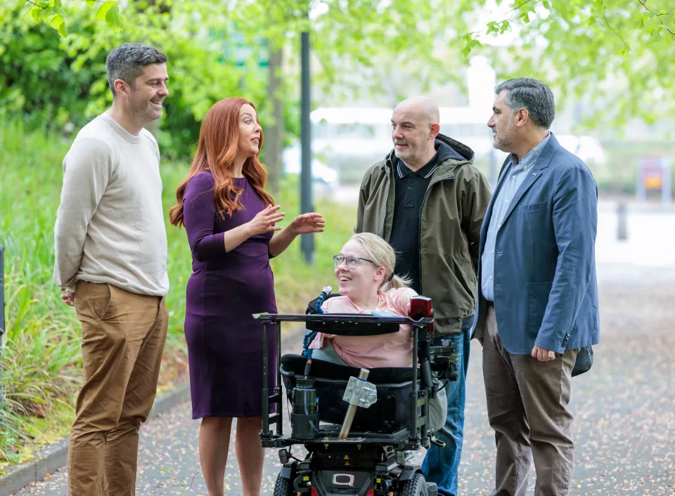 Group of three men men and two women gathered talking. One woman is in a wheelchair