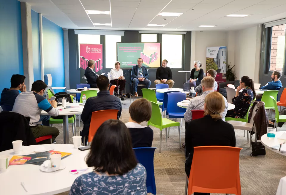 Groups of people sitting at round tables looking towards a four person panel