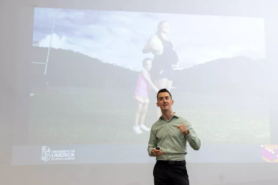 Man presenting with image of woman and girl projected onto screen in the background