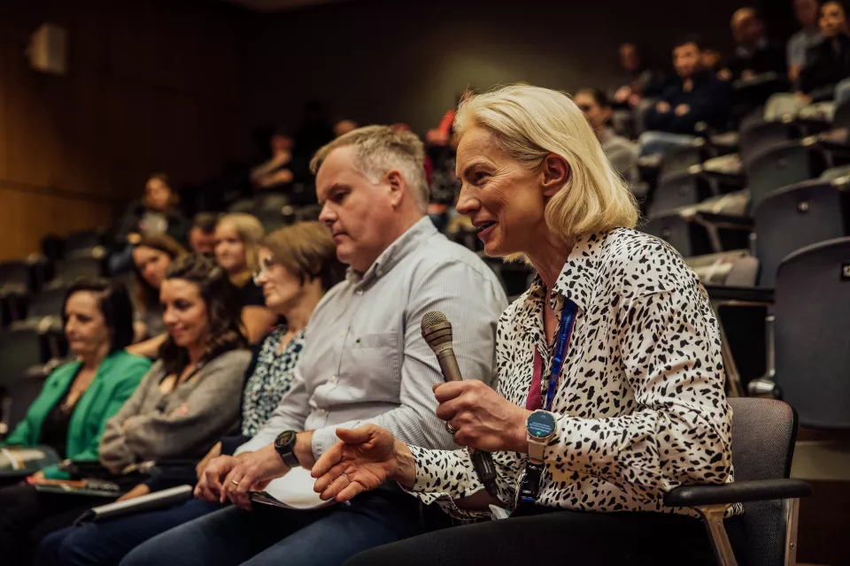 Members of an audience with one woman in foreground holding a microphone