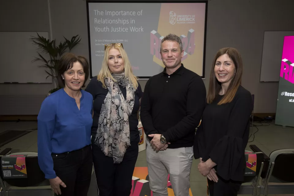 Three women and one man standing together with lecture theatre in background