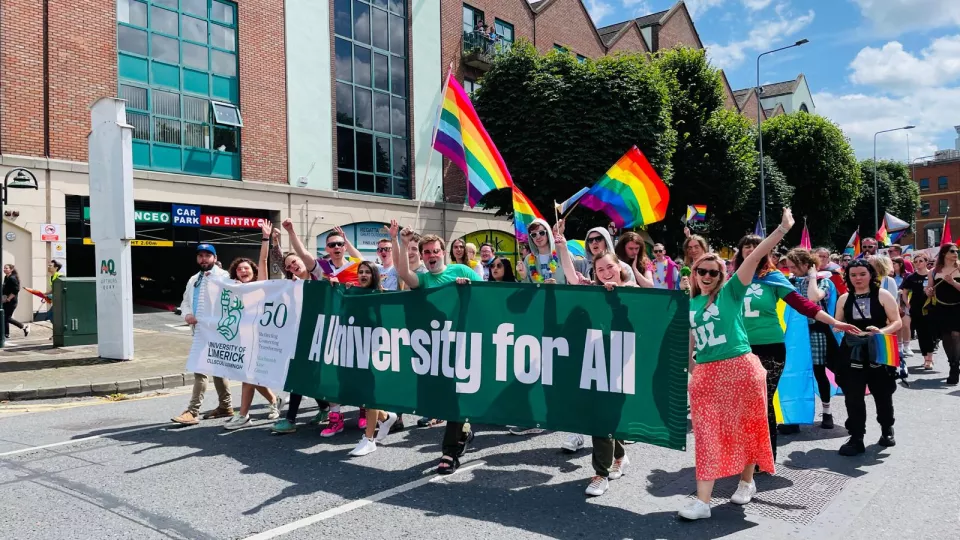 A parade with people holding a "A University for All" banner and waving rainbow flags.